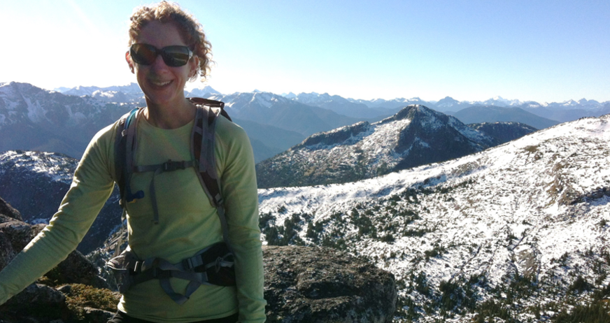 Person hiking in snowy mountains with blue sky and distant peaks in the background.